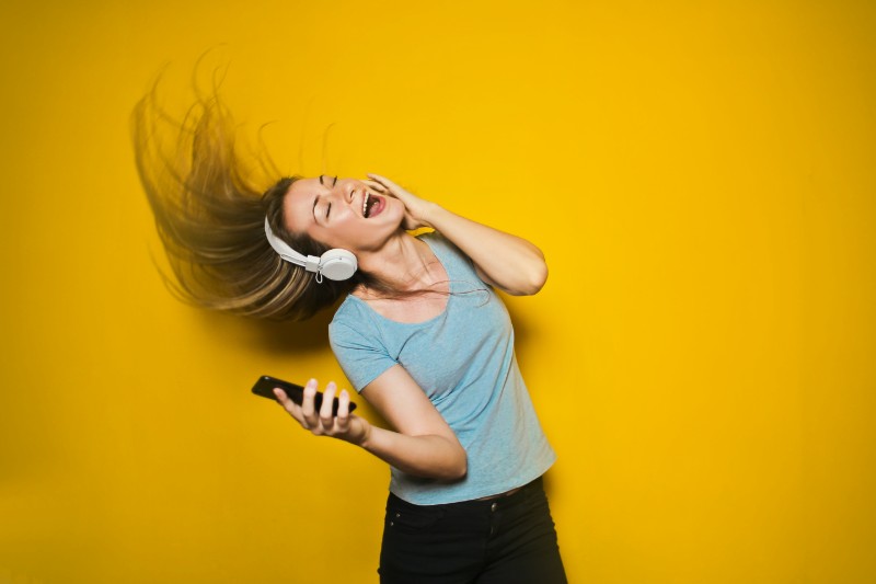 girl singing with headphones on yellow backfground